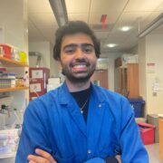 Riaz Mowzoon-Mogharrabi in a blue lab coat standing in front of a lab workstation